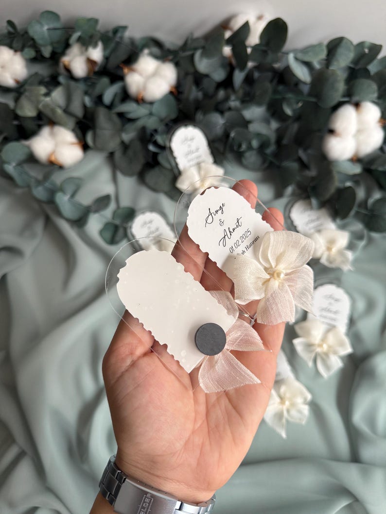 May include: Clear plastic favor boxes with white paper inserts and white ribbon bows. The boxes have the text "Sinem & Ahmet 01.02.2025 In Istanbul" printed on them.