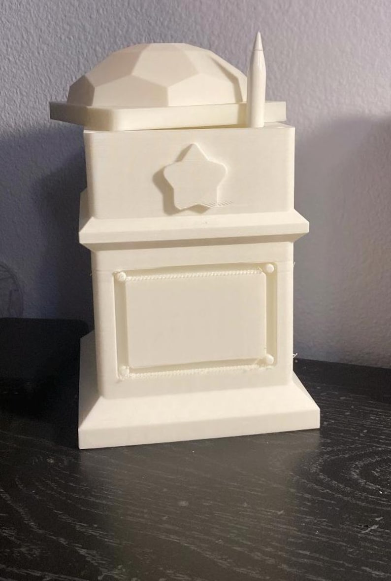 May include: White 3D printed box with a star on the front and a blank rectangular space. The box has a removable lid with a geometric design.
