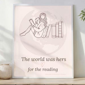 Puede incluir: Una impresión enmarcada con un dibujo lineal minimalista de una persona leyendo, con el texto "The world was hers for the reading." La obra de arte presenta un fondo rosa suave con un contorno de globo. La impresión se exhibe sobre una superficie de madera con jarrones decorativos y una planta en maceta.