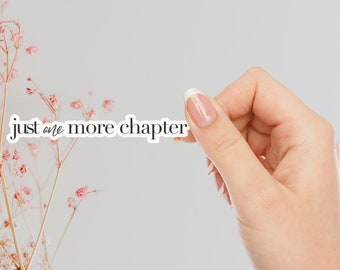 May include: A white sticker with the text "just one more chapter" on a white background. A hand is holding the sticker.