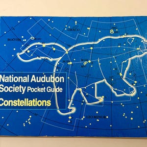 May include: A blue "National Audubon Society Pocket Guide Constellations" book. The cover features a white outline of a bear constellation, with connecting lines and star names. The book is designed for educational purposes.