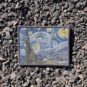 Op de afbeelding: Geborduurde patch met Van Goghs "Sterrennacht" schilderij. De patch toont de wervelende blauwe nachthemel met gele sterren en een hoge, donkere cipres. De patch heeft een donkerblauwe rand en is rechthoekig van vorm.