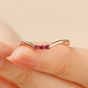 May include: A delicate gold ring with a curved band and three small pink gemstones.