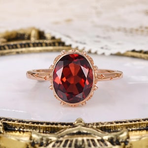 Op de afbeelding: Een ring van roségoud met een ovale rode granaatsteen, gezet in een delicate, sierlijke setting.