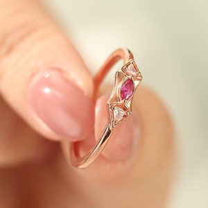 Könnte beinhalten: Ein zarter Ring aus Roségold mit einem rosafarbenen, marquiseförmigen Edelstein, der von kleineren, klaren Edelsteinen umgeben ist.
