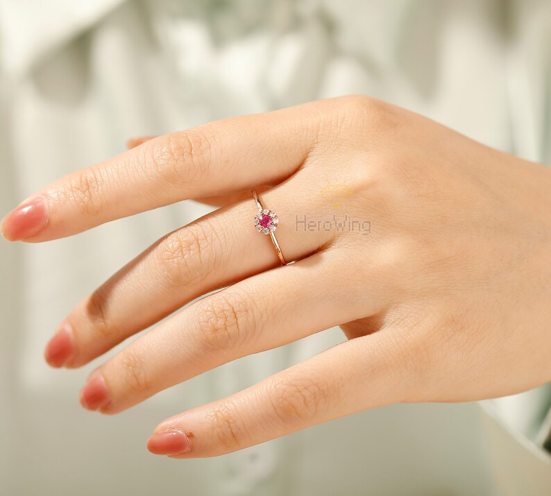 K&ouml;nnte beinhalten: Ein Ring aus Ros&eacute;gold mit einem kleinen roten Edelstein, der von einem Heiligenschein aus kleineren wei&szlig;en Edelsteinen umgeben ist.