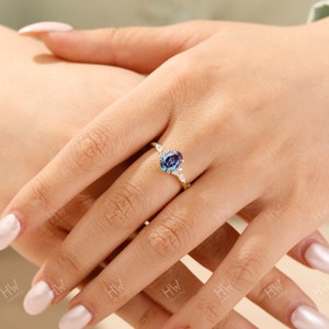 May include: A gold ring featuring a large, oval-cut, color-changing alexandrite gemstone. The ring is accented with smaller, round, white gemstones on either side of the main stone. The ring's band is a delicate gold color.