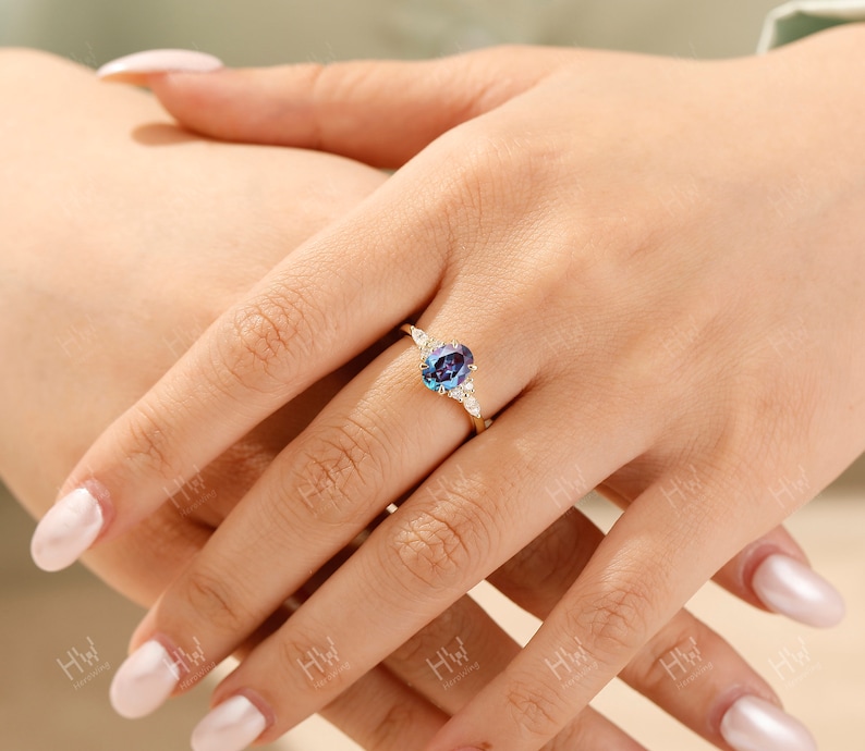 May include: A gold ring featuring a large, oval-cut, color-changing alexandrite gemstone. The ring is accented with smaller, round, white gemstones on either side of the main stone. The ring's band is a delicate gold color.