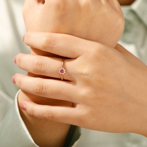 K&ouml;nnte beinhalten: Ein Ring aus Ros&eacute;gold mit einem roten Edelstein, der von kleineren wei&szlig;en Edelsteinen umgeben ist.