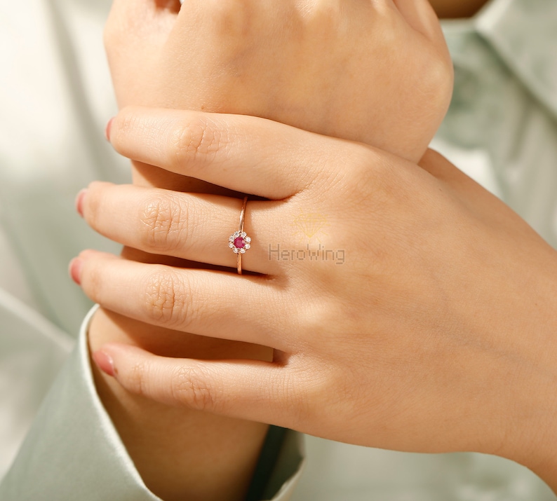 K&ouml;nnte beinhalten: Ein Ring aus Ros&eacute;gold mit einem roten Edelstein, der von kleineren wei&szlig;en Edelsteinen umgeben ist.