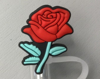 May include: A red rose-shaped charm with a black outline and light blue leaves. The charm is attached to a clear plastic straw topper with a white loop. The rose is the focal point, with detailed petals.