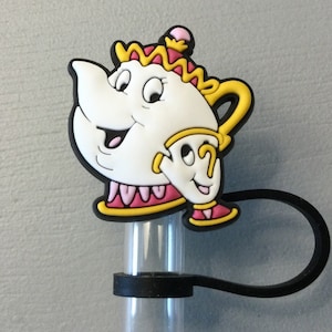 May include: A white, yellow, pink, and black cartoon teapot and teacup character design. The character is attached to a clear plastic tube with a black loop. The design is a whimsical, animated character.