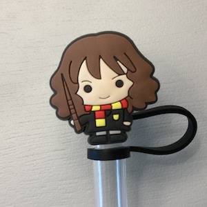 May include: A brown and black character with brown hair holding a wand, wearing a red and yellow scarf and a black robe. The character is attached to a black silicone straw holder.