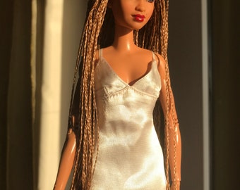 May include: A doll with long, braided, light brown hair wearing a white satin slip dress.