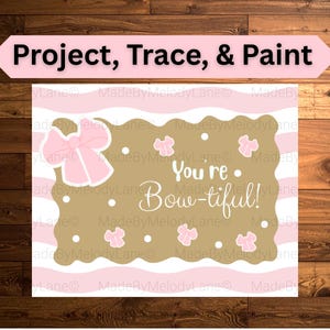 May include: A pink and gold art print featuring the phrase "You're Bow-tiful!" and bow illustrations. The print is framed with pink and white stripes and has the words "Project, Trace, & Paint" at the top.