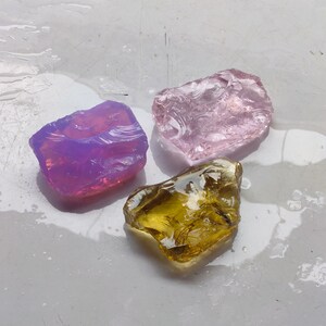 Pode incluir: Três peças de vidro transparente, uma roxa, uma rosa e uma amarela, com uma superfície texturizada.