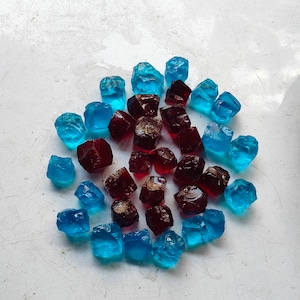 May include: A collection of blue and red glass gems arranged in a circle on a white surface.
