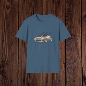 Puede incluir: Una camiseta azul con un gráfico de coche vintage impreso en la parte delantera. El coche es gris y blanco y tiene una franja negra a lo largo del lateral. El fondo del gráfico es azul claro con rayas blancas.