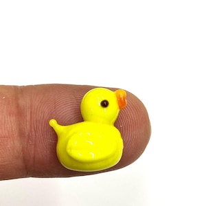 May include: A small yellow glass duck figurine with a black eye and an orange beak.