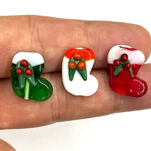 May include: Three glass Christmas stocking ornaments. The ornaments are red, white, and green. Each ornament has a sprig of holly with red berries.