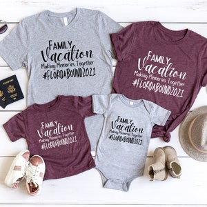May include: A set of four t-shirts with the text "Family Vacation Making Memories Together #FLORIDABOUND2021" printed on them. The shirts are in two colours: grey and maroon. The shirts are arranged on a white wooden surface with accessories such as sunglasses, a hat, and passports.
