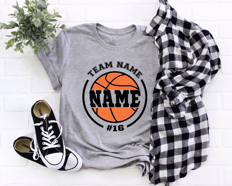 May include: Gray t-shirt with a black and orange basketball graphic. The basketball has the text "TEAM NAME" above it and "NAME" inside the basketball. The number "#16" is below the basketball.