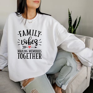May include: White sweatshirt with black text that reads "FAMILY vibes MAKING MEMORIES TOGETHER" with a red heart above the word "vibes".