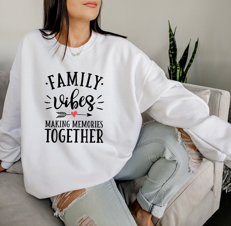 May include: White sweatshirt with black text that reads "FAMILY vibes MAKING MEMORIES TOGETHER" with a red heart above the word "vibes".