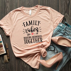 May include: A peach-colored t-shirt with the text "FAMILY vibes MAKING MEMORIES TOGETHER" in black lettering with a red heart and arrow graphic.