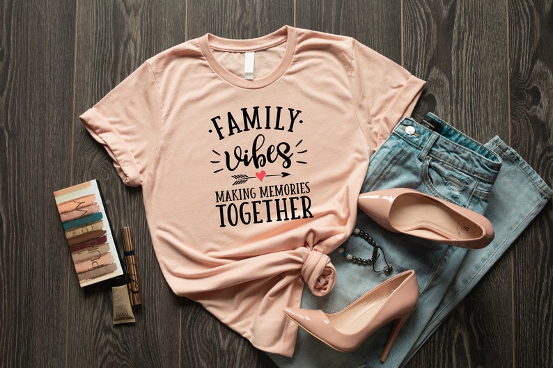 May include: A peach-colored t-shirt with the text "FAMILY vibes MAKING MEMORIES TOGETHER" in black lettering with a red heart and arrow graphic.