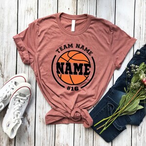 May include: A mauve t-shirt with a black basketball graphic and the text "TEAM NAME NAME #16".