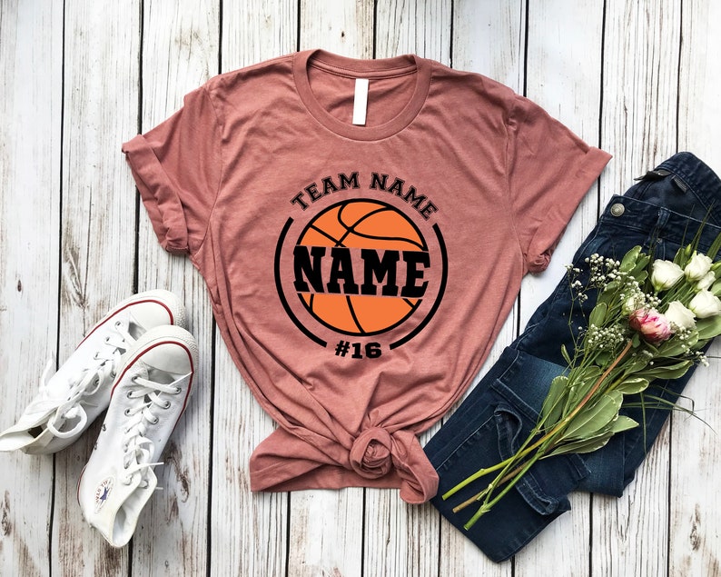 May include: A mauve t-shirt with a black basketball graphic and the text "TEAM NAME NAME #16".