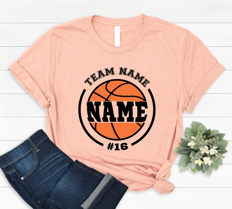 May include: A peach-colored t-shirt with a black and orange basketball graphic. The graphic includes the text "TEAM NAME" and "NAME" with the number "#16" below the basketball.