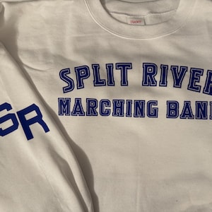 May include: White sweatshirt with blue lettering that reads "Split River Marching Band." The sleeve features the letters "SR" in blue. The sweatshirt is made of a soft material and is likely for a school or band.