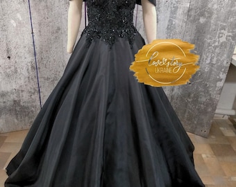 May include: A floor-length black gown featuring an off-the-shoulder neckline with draped sleeves and a sweetheart bodice adorned with intricate black beadwork and sequins. The skirt is full and voluminous, extending to the floor in a solid black fabric.