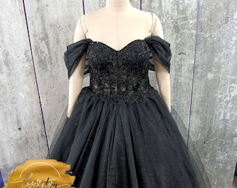 May include: A black tulle ball gown with a sweetheart neckline and off-the-shoulder straps. The bodice is embellished with black beading and lace. The skirt is full and flowing.