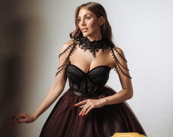 May include: A black corset-style bodice with a burgundy tulle skirt. The dress features a black lace collar with beaded shoulder accents. The overall design is elegant and suitable for formal events.