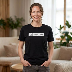 May include: Black t-shirt with the text "I am not a robot" inside a white rectangle with a tick. The person is wearing the t-shirt and is standing in front of a neutral background.