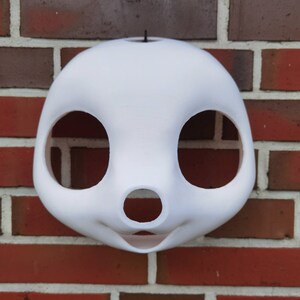 May include: White unfinished furry animal mask with large eye holes and a small nose hole. The mask is made of a smooth, hard material and has a hole at the top for attaching a strap.