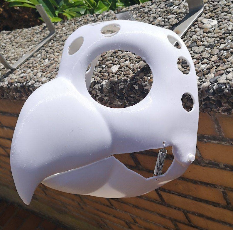 May include: White plastic mask with a beak and multiple holes. A small metal spring is attached to the bottom of the mask.