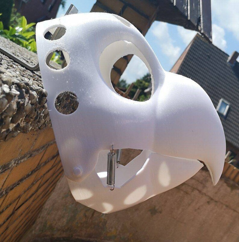May include: White plastic mask with a beak and multiple holes. The mask is attached to a metal spring.