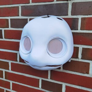 May include: White plaster mask with two large eye holes and a small mouth opening. The mask is unfinished and has a rough texture.