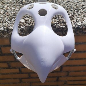May include: White plastic mask with a bird-like beak and multiple holes for eyes and nose. The mask is designed to be worn over the face.