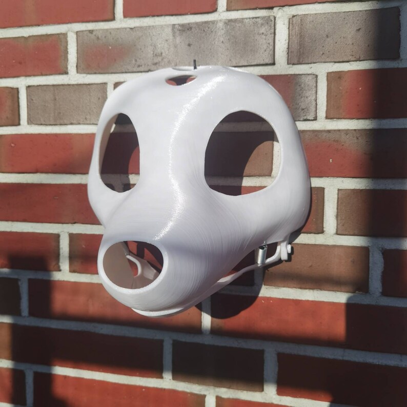May include: White 3D printed animal mask with holes for eyes and nose. The mask is hanging on a brick wall.