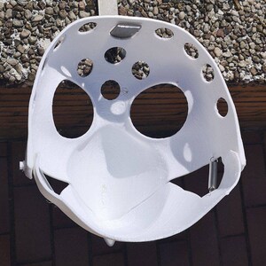 May include: White plastic helmet with multiple holes and a spring attached to the side.