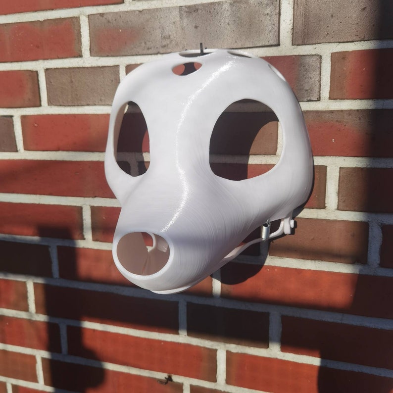 May include: White 3D printed animal mask with holes for eyes and nose. The mask is hanging on a brick wall.