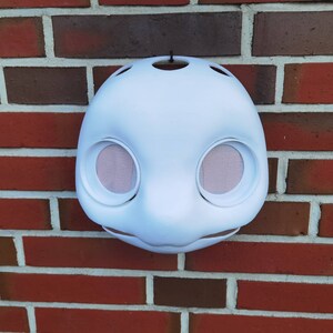 May include: White unfinished plaster mask with two large eye holes. The mask is a blank canvas for painting or decorating.