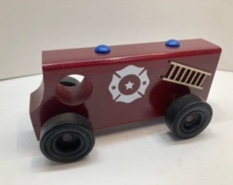 May include: A red wooden toy fire truck with black wheels, a ladder on the side, and a white fire department emblem with a star on the front.