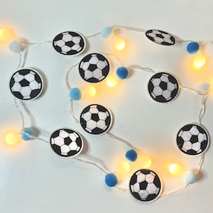 May include: A string of white lights with blue and white pom-poms and black and white soccer ball ornaments.