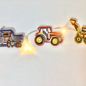 May include: A string of white fairy lights with yellow bulbs, decorated with felt patches of a red tractor, a blue dumper truck, and a yellow excavator.